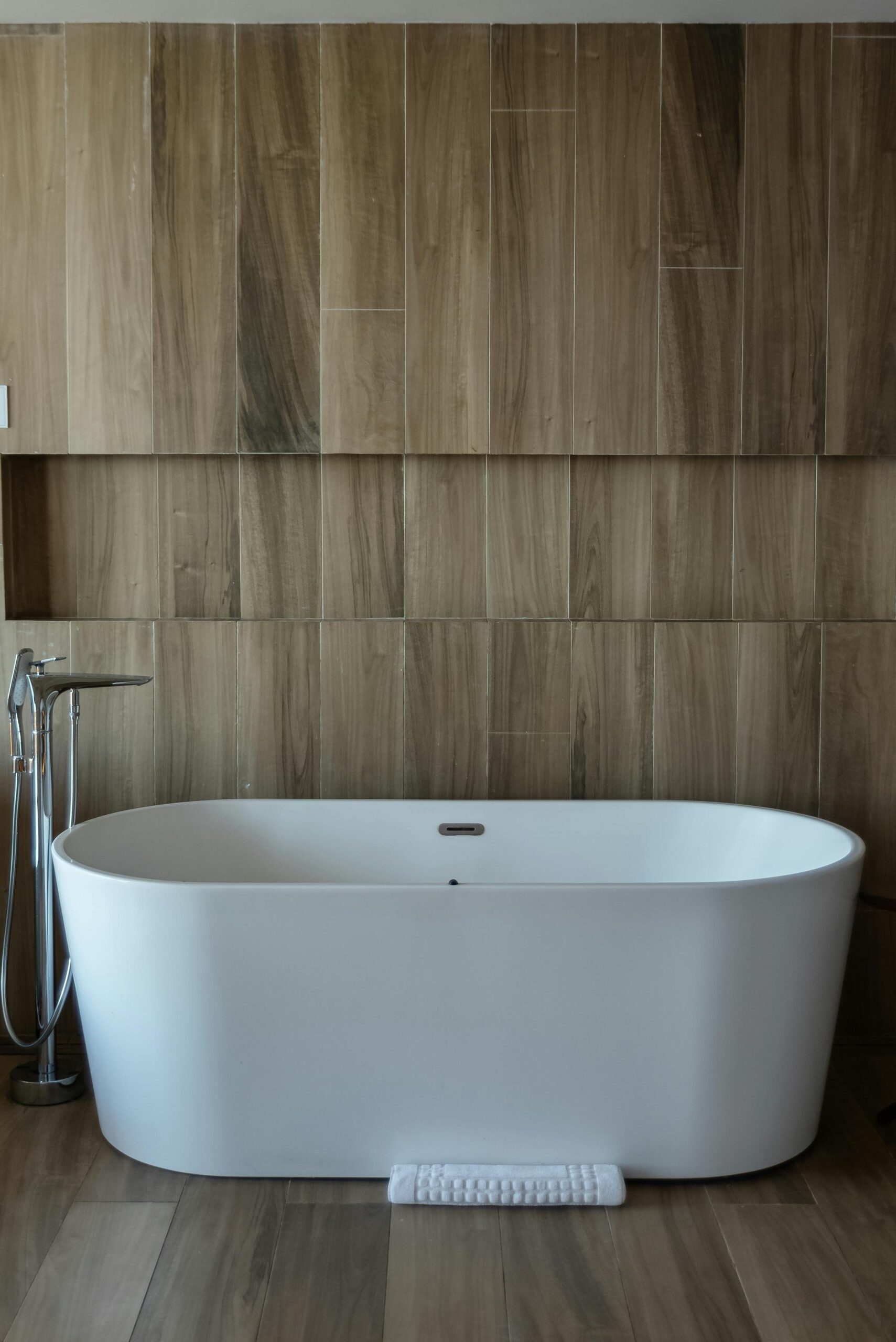 A stylish white bathtub in a contemporary spa-like bathroom with wooden decor.